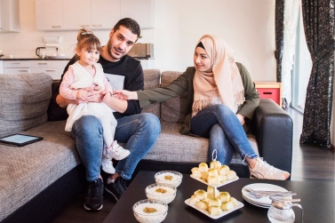 Twee personen zitten samen met een kind op de bank.